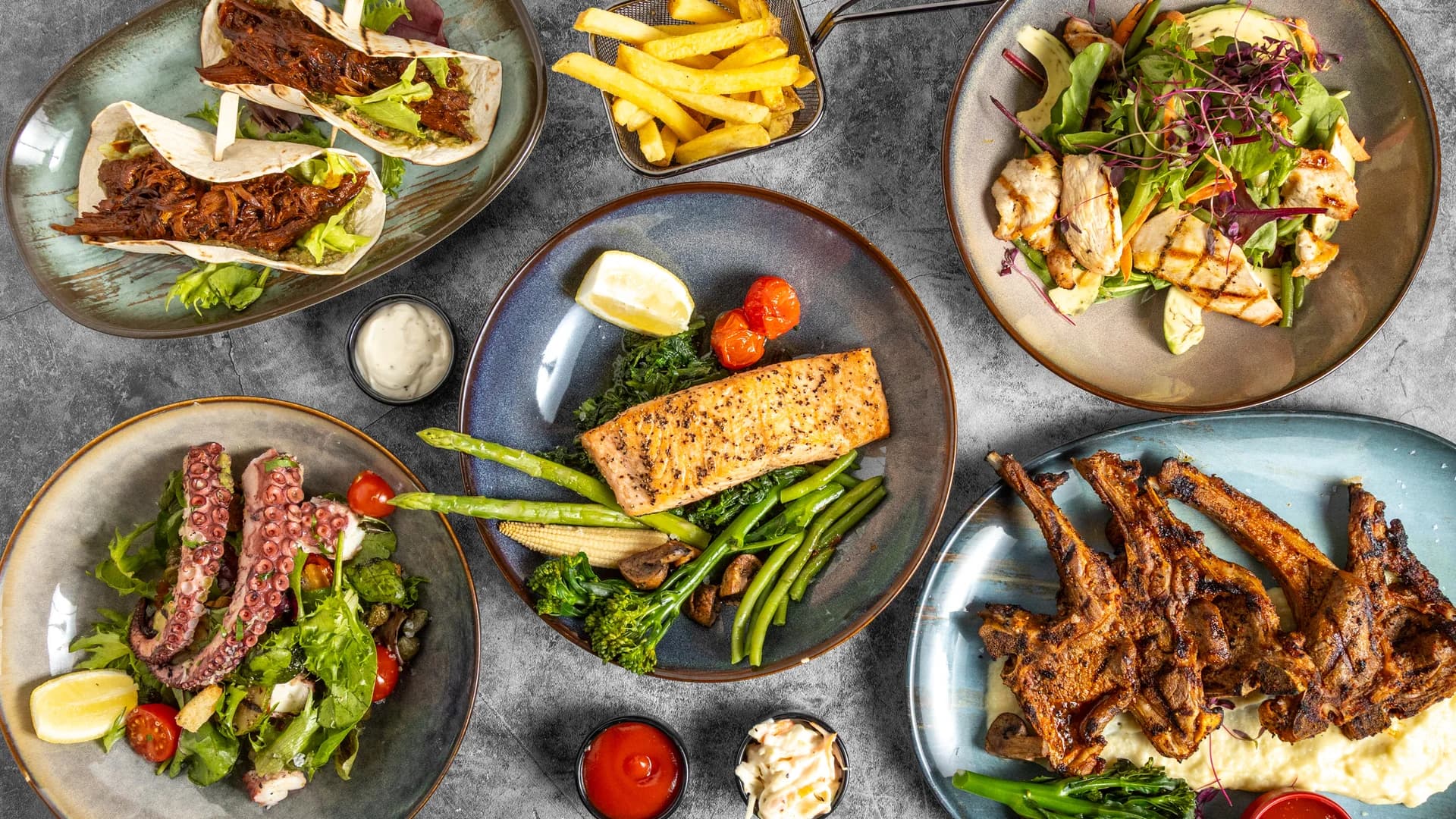 Prime Fire grilled dishes, salads and tacos arranged around the table
